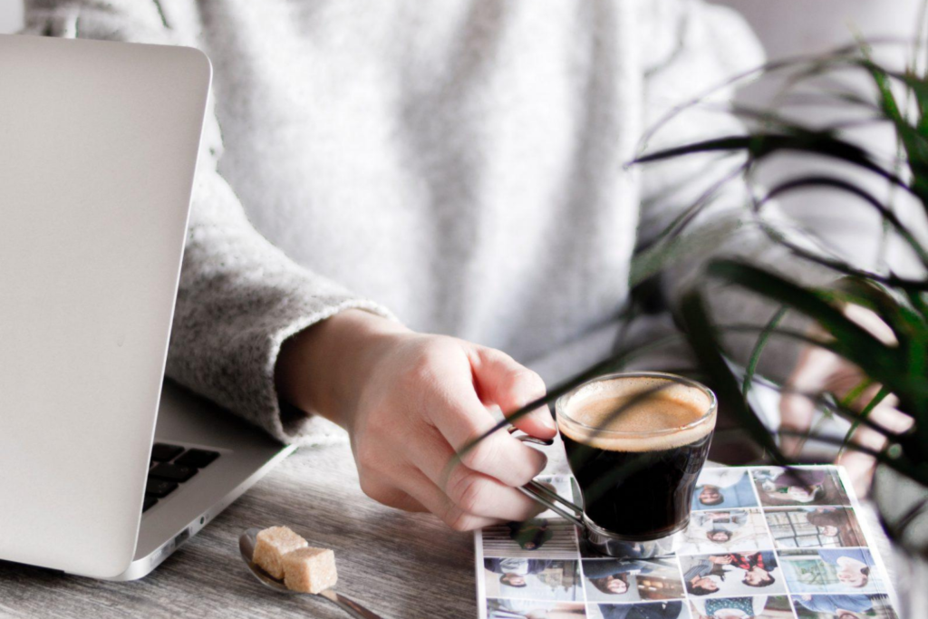 A woman holding a cup of coffee next to her laptop