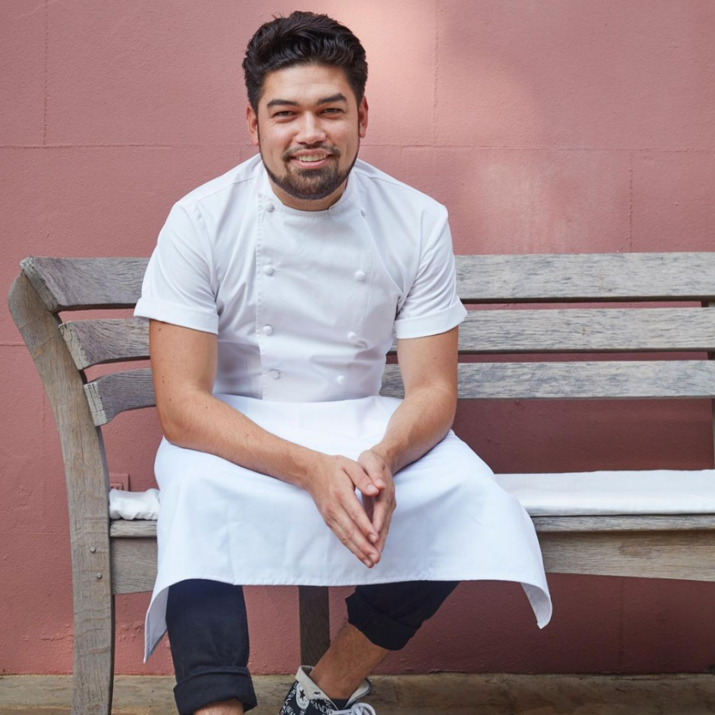 Luke Selby in his chef whites sat in front of a pink wall