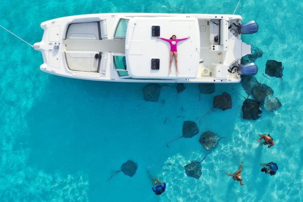 Travel inspiration: a girl in a pink top lying on a boat surrounded by stingrays on Grand Cayman