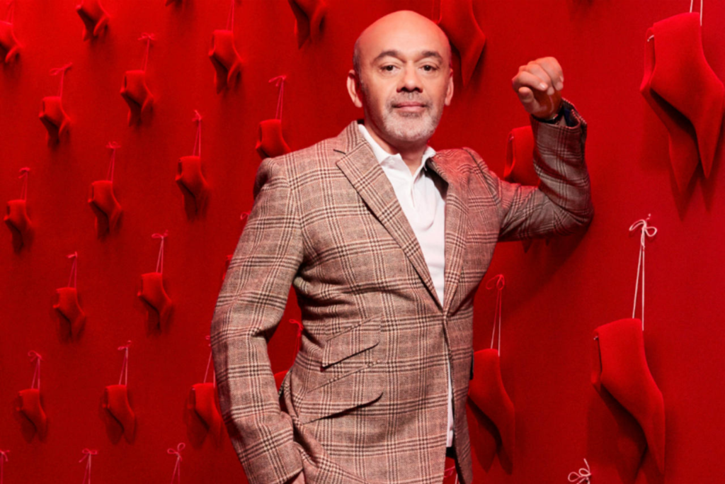 Christian Louboutin in front of a red wall of red shoes